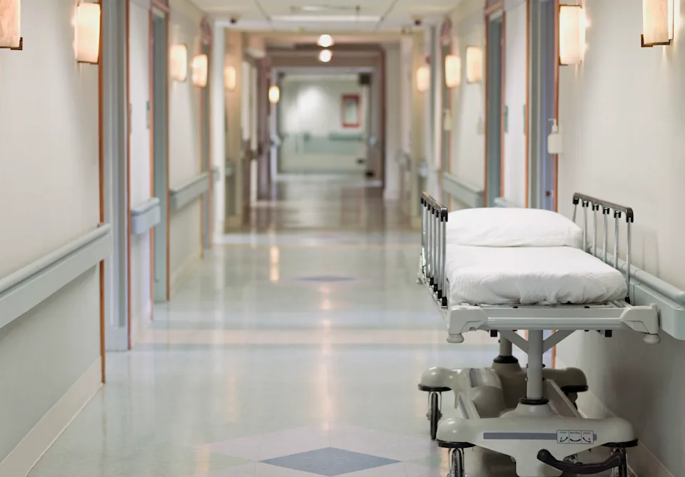 A clinician walking down a hospital hallway outside an oncology or gastroenterology unit, candid documentary-style photograph