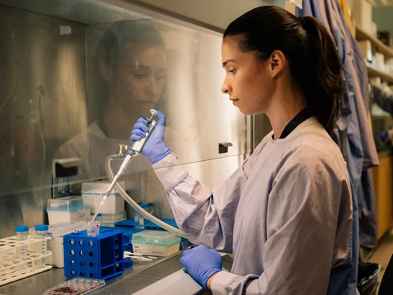 A laboratory technician in protective equipment working at a bench with medical sample tubes in a cancer research lab, realistic photograph