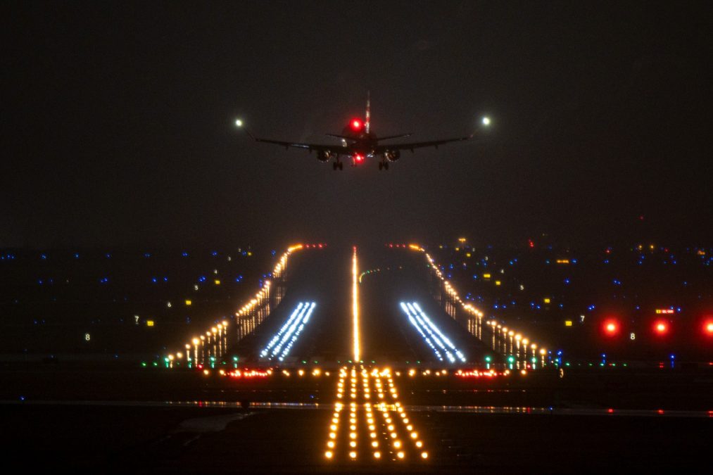 A nighttime photograph of a commercial airplane in flight with visible navigation lights against a dark sky