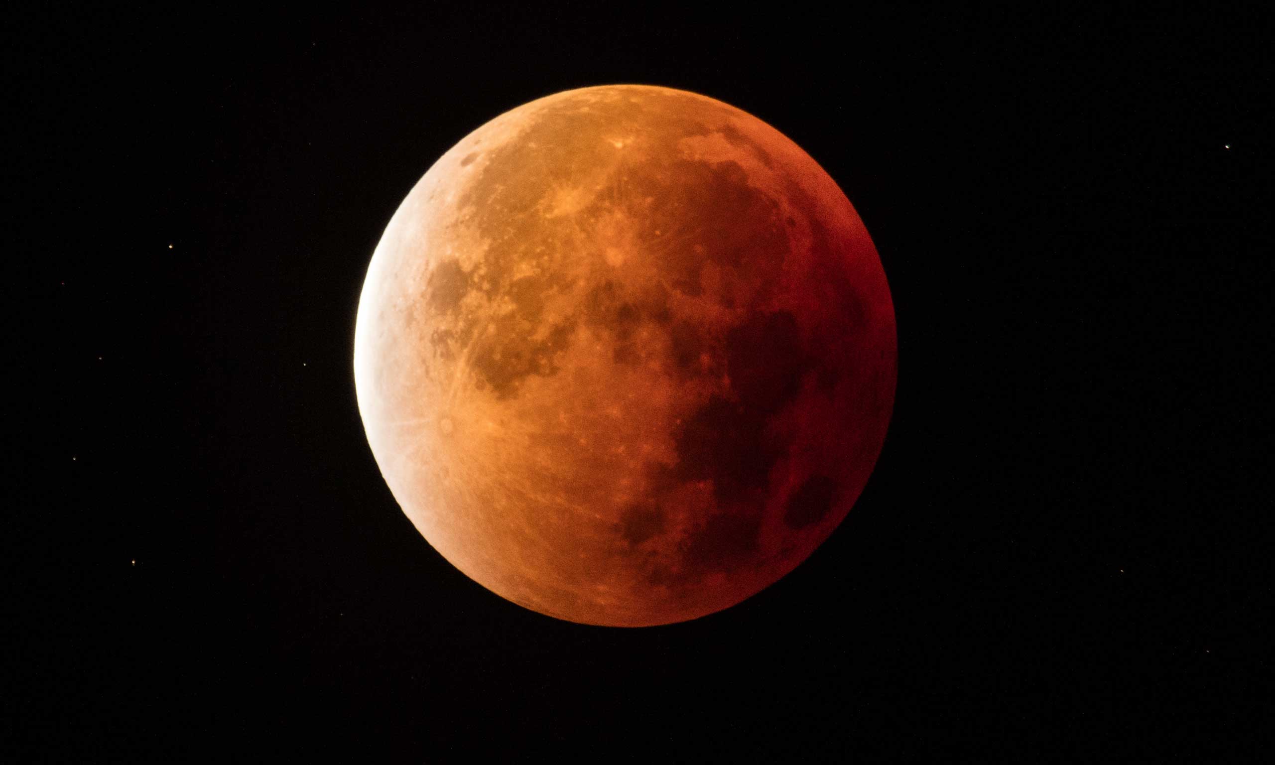 A real photograph of a total lunar eclipse with the Moon appearing dark red and slightly dim against a starry night sky