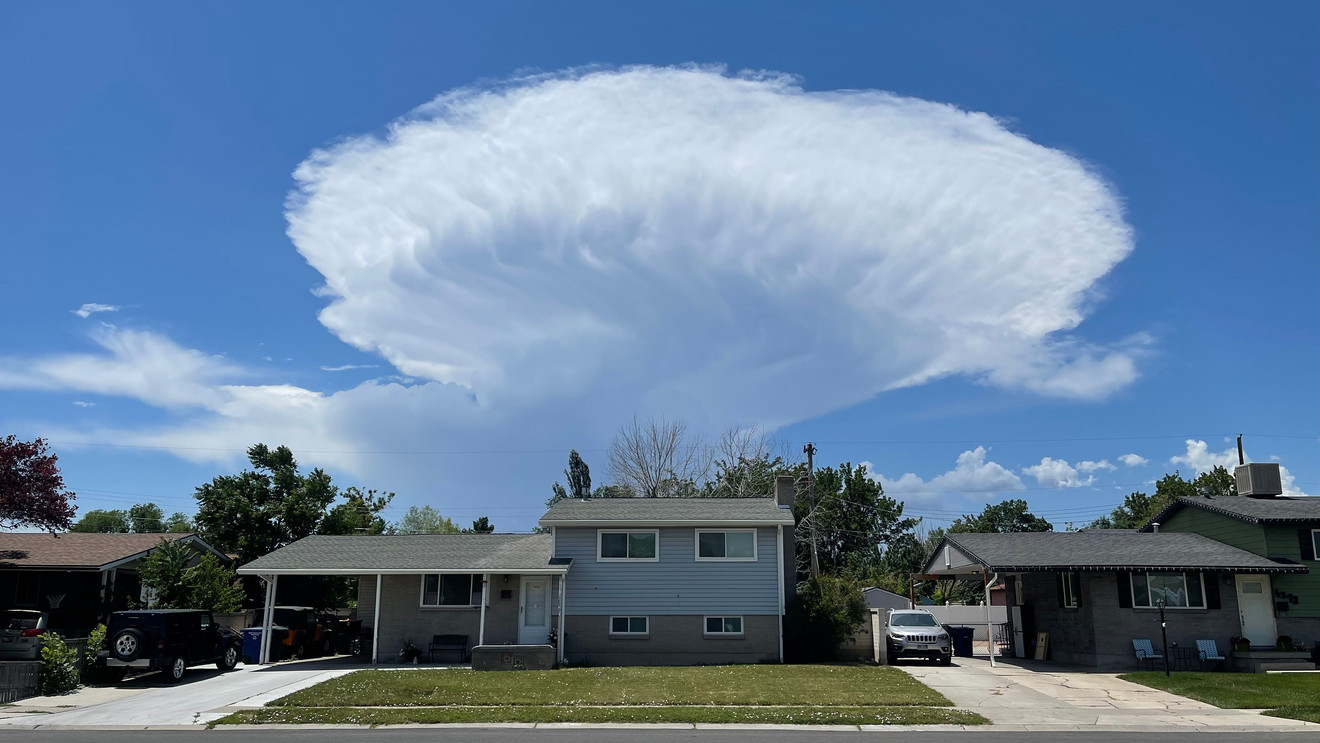A towering cumulonimbus thunderstorm cloud with a wide anvil top spreading across a blue sky