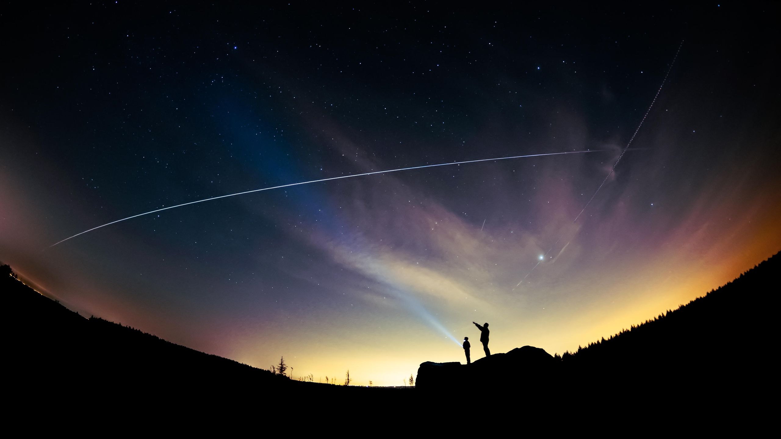 A wide night sky photo with the International Space Station appearing as a bright moving point above a dark horizon