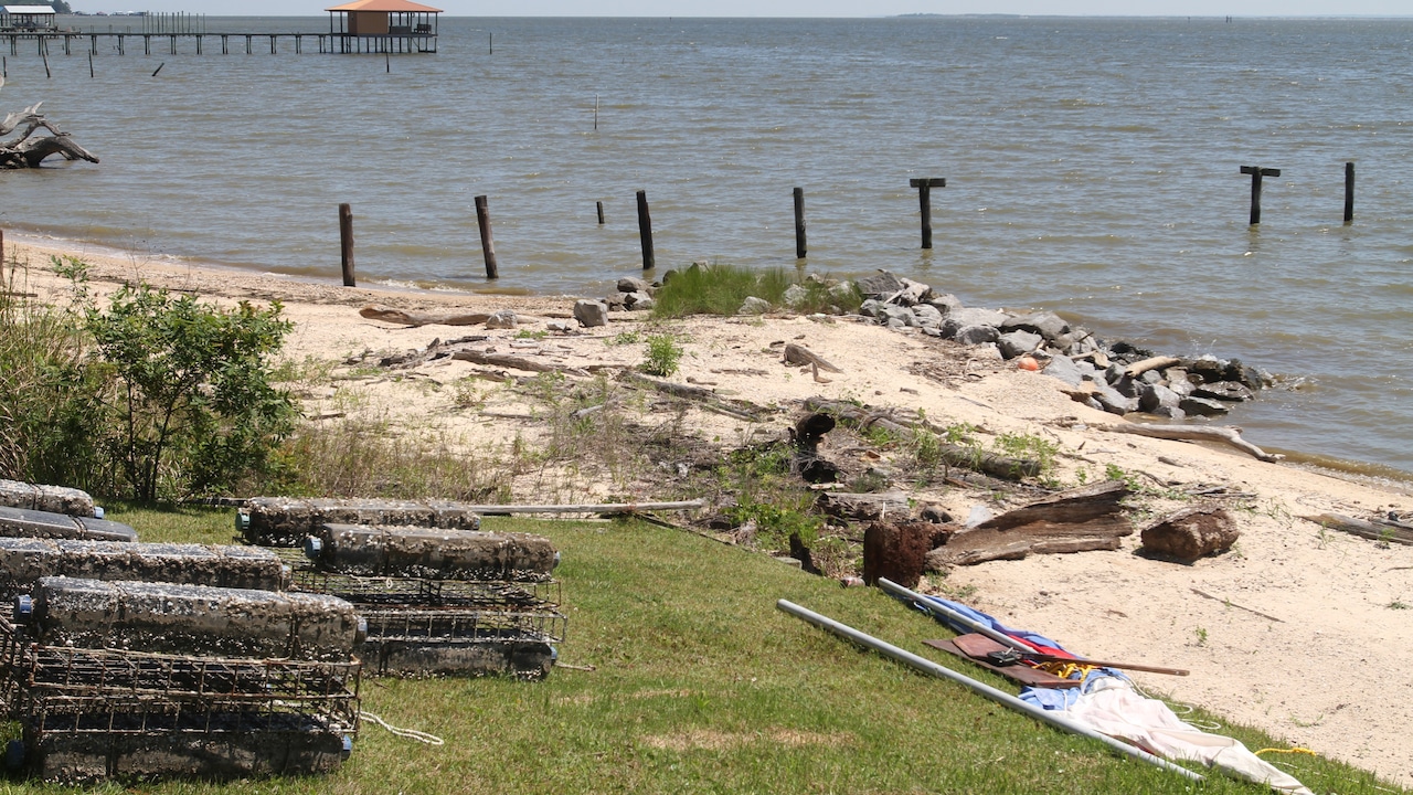 High waves and rising water along the shoreline of Mobile Bay as storm conditions build, with wind-driven spray near coastal structures
