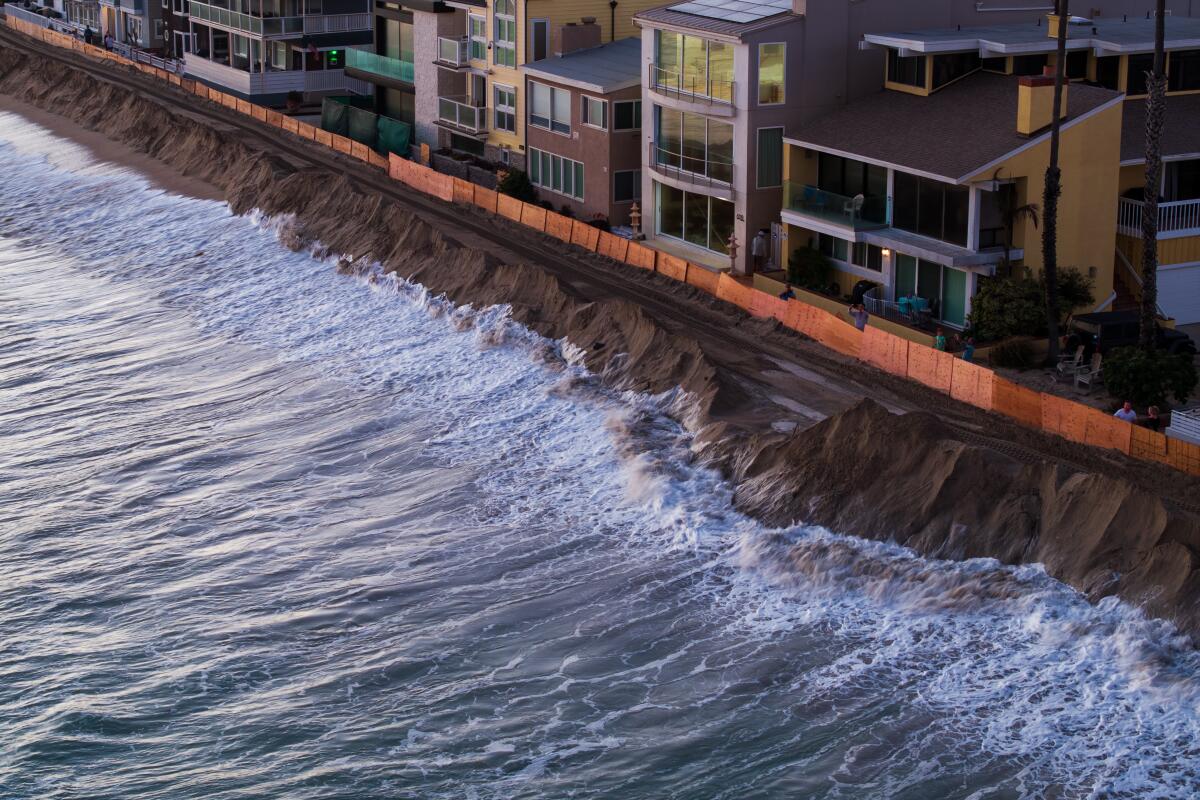 Ocean water washing over a low-lying coastal walkway in California during a peak high tide on a clear day, with wet pavement and small pooled seawater visible