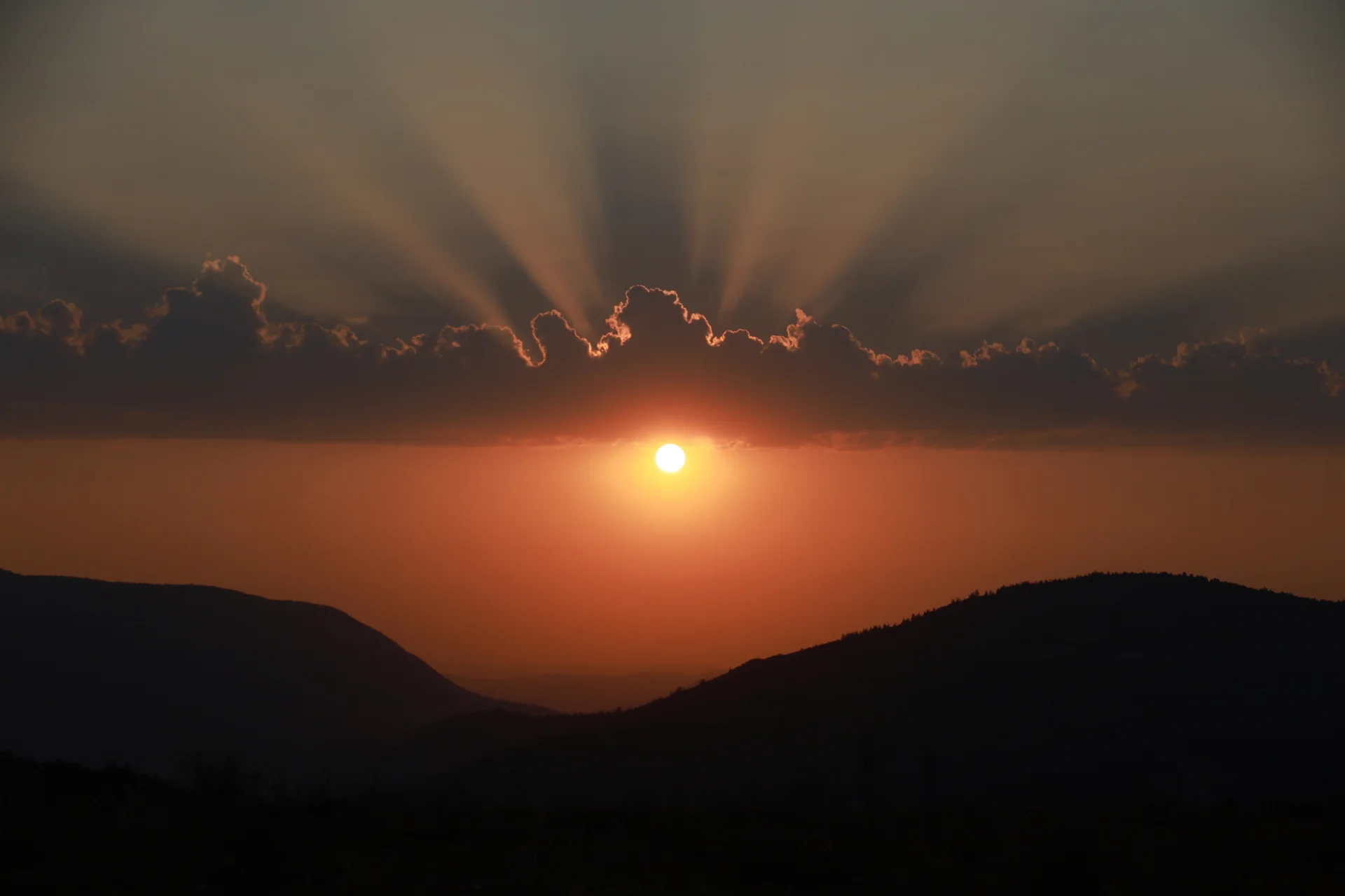 Sunbeams streaming through gaps in clouds at sunset with warm orange light near the horizon