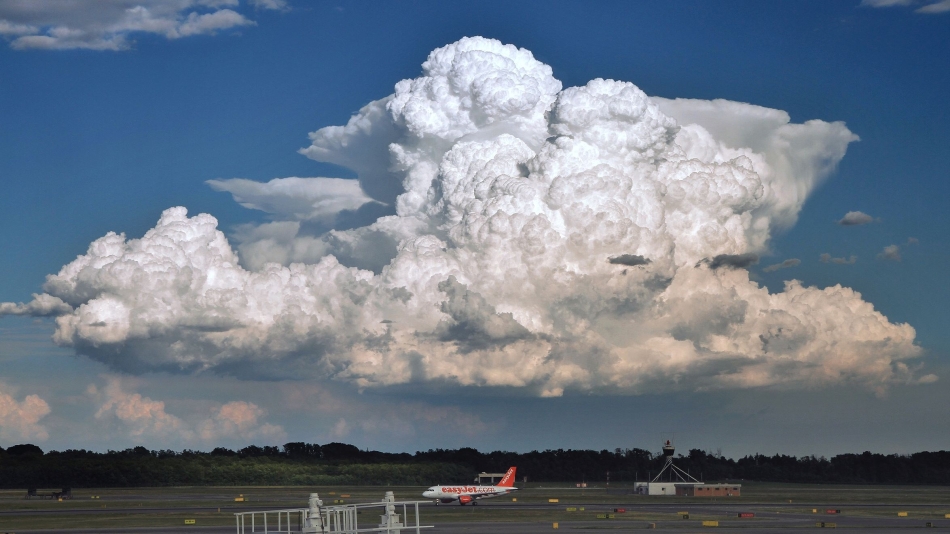 The dark, textured base of a cumulonimbus thunderstorm cloud hanging low over a flat landscape, with visible rain shafts in the distance
